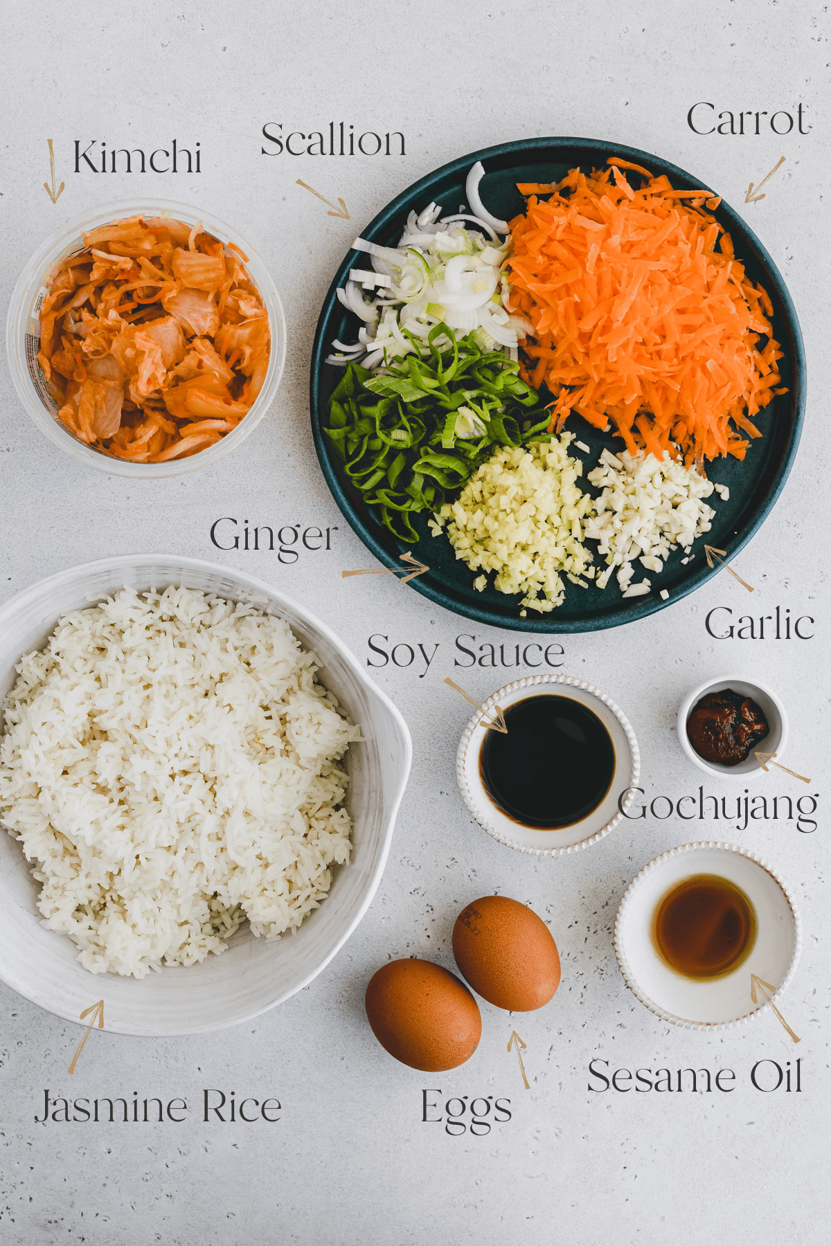 Top view of ingredients of Kimchi Fried Rice including kimchi, ginger, garlic, soy sauce, gochujang, eggs, carrots, scallions, jasmine rice and sesame oil.