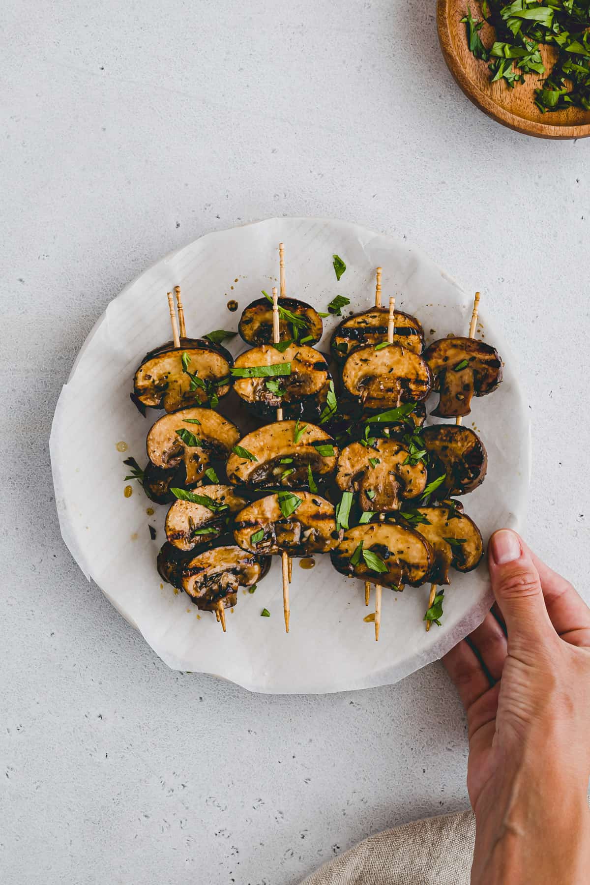 a hand holding a plate with grilled mushroom skewers