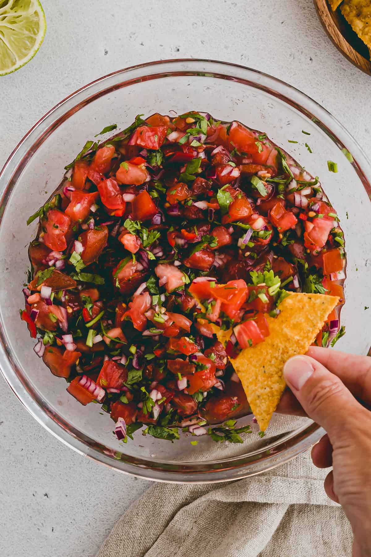 a hand dipping a nacho into pico de gallo sauce