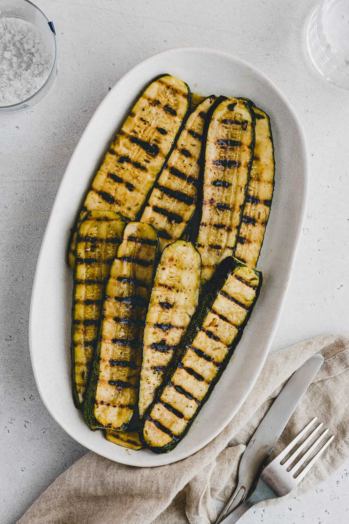 Grilled slices of zucchini in a single layer on a white oval plate.