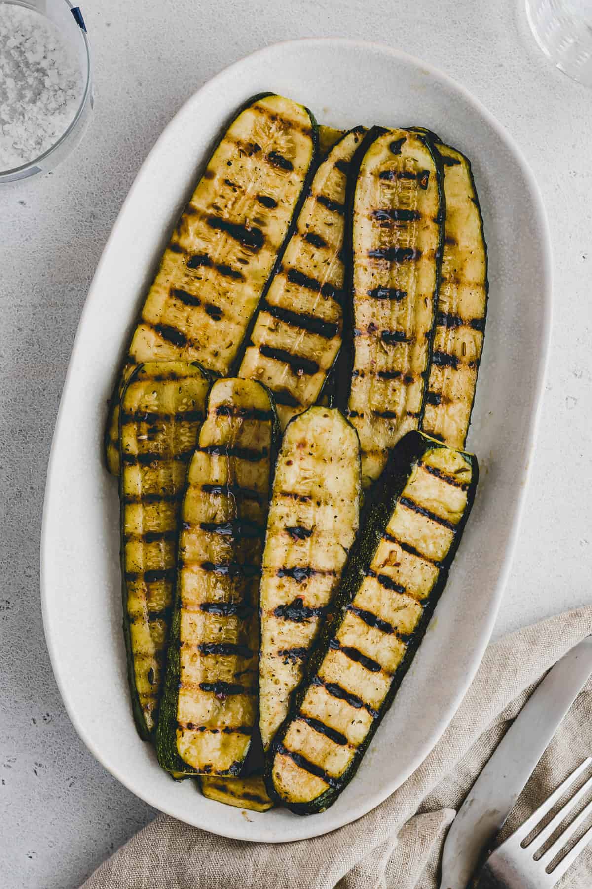Top view of grilled zucchini slices on a white oval pate. 