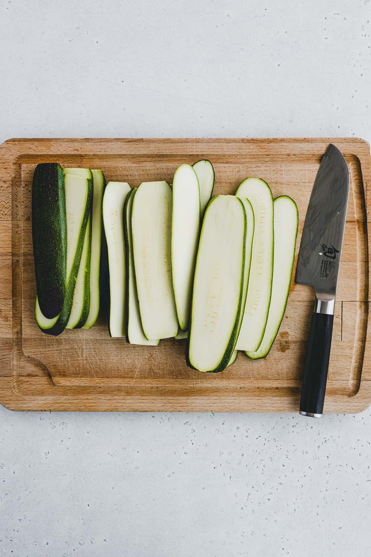 Top view of slices of zucchini on a chopping board with a knife next to them. 