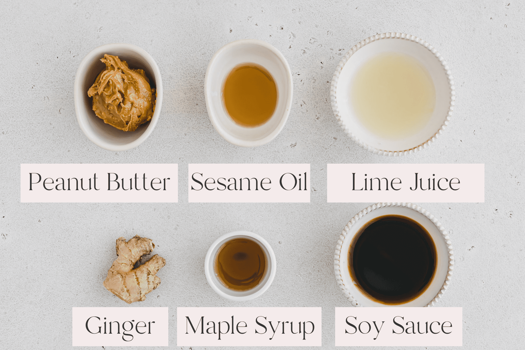 Top view of Asian Peanut Dressing Ingredients including small bowls with peanut butter, sesame oil, lime juice, maple syrup and soy sauce, with a ginger root on the table next to the bowls. 