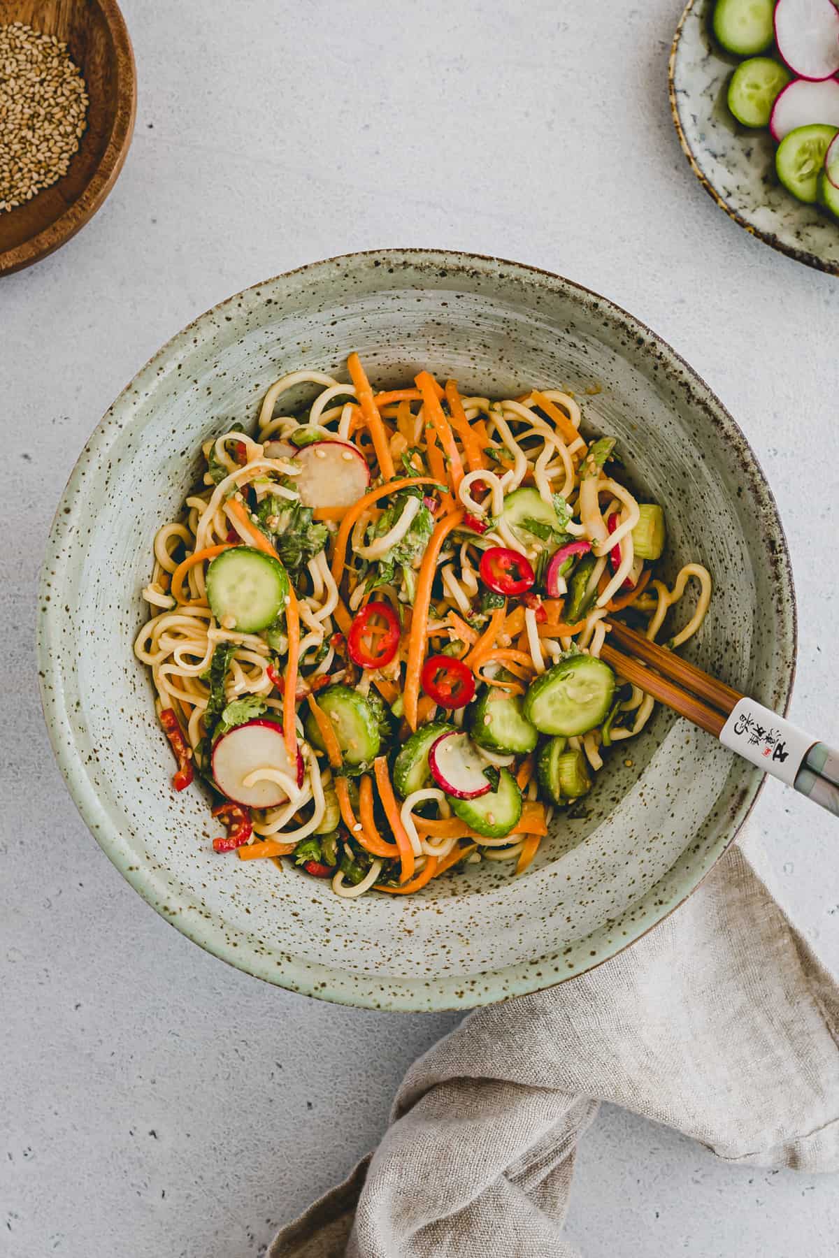 Top view shot of Asian noodle salad in a round grey spotted plate with chopsticks sitting on the side of the plate. 