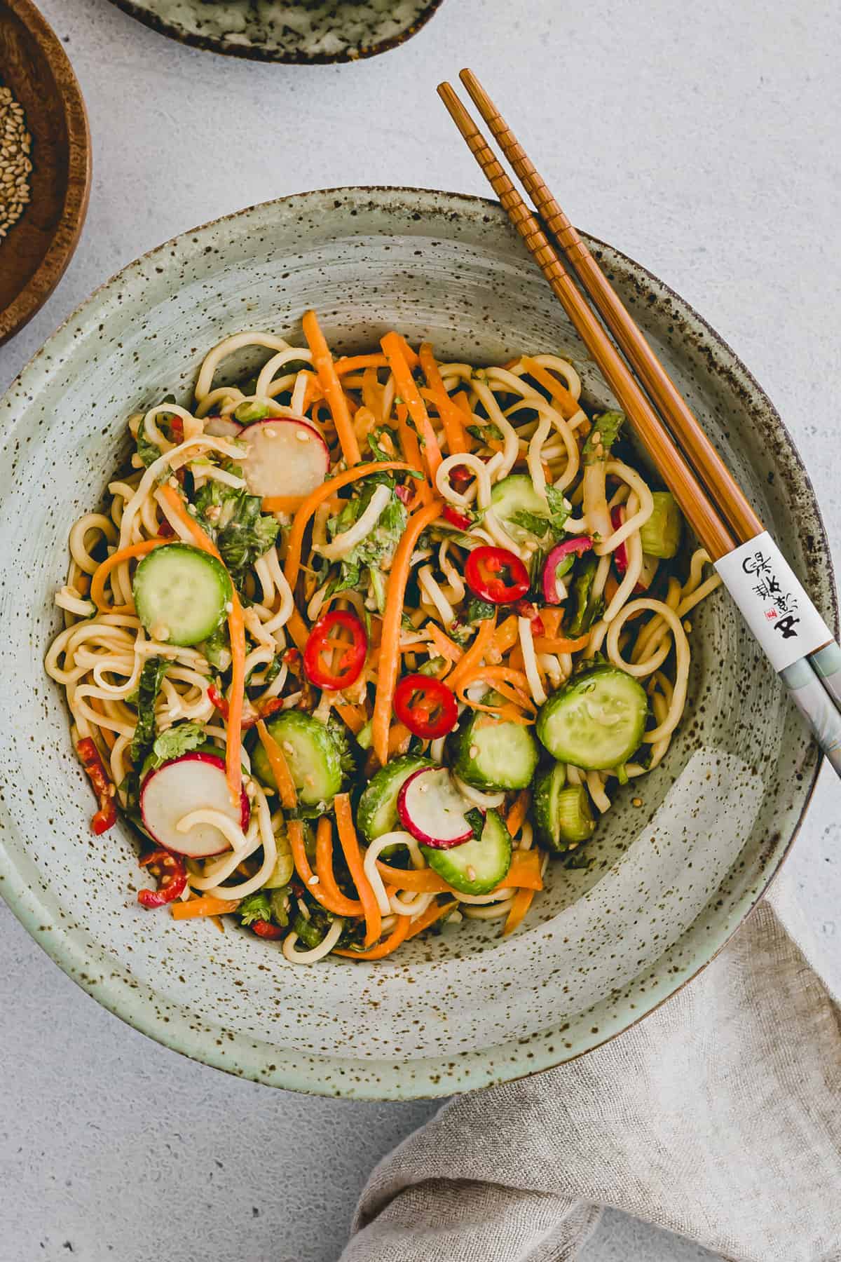 Hero shot with a top view close-up of Asian noodle salad on a round grey spotted plate with chopsticks sitting on the side of the plate. 