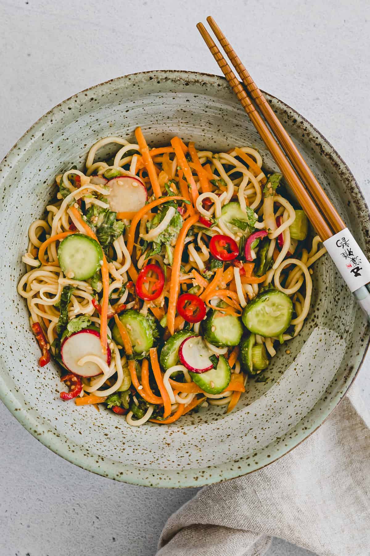 Top view close-up shot of Asian noodle salad on a round grey spotted plate with chopsticks sitting on the side of the plate. 