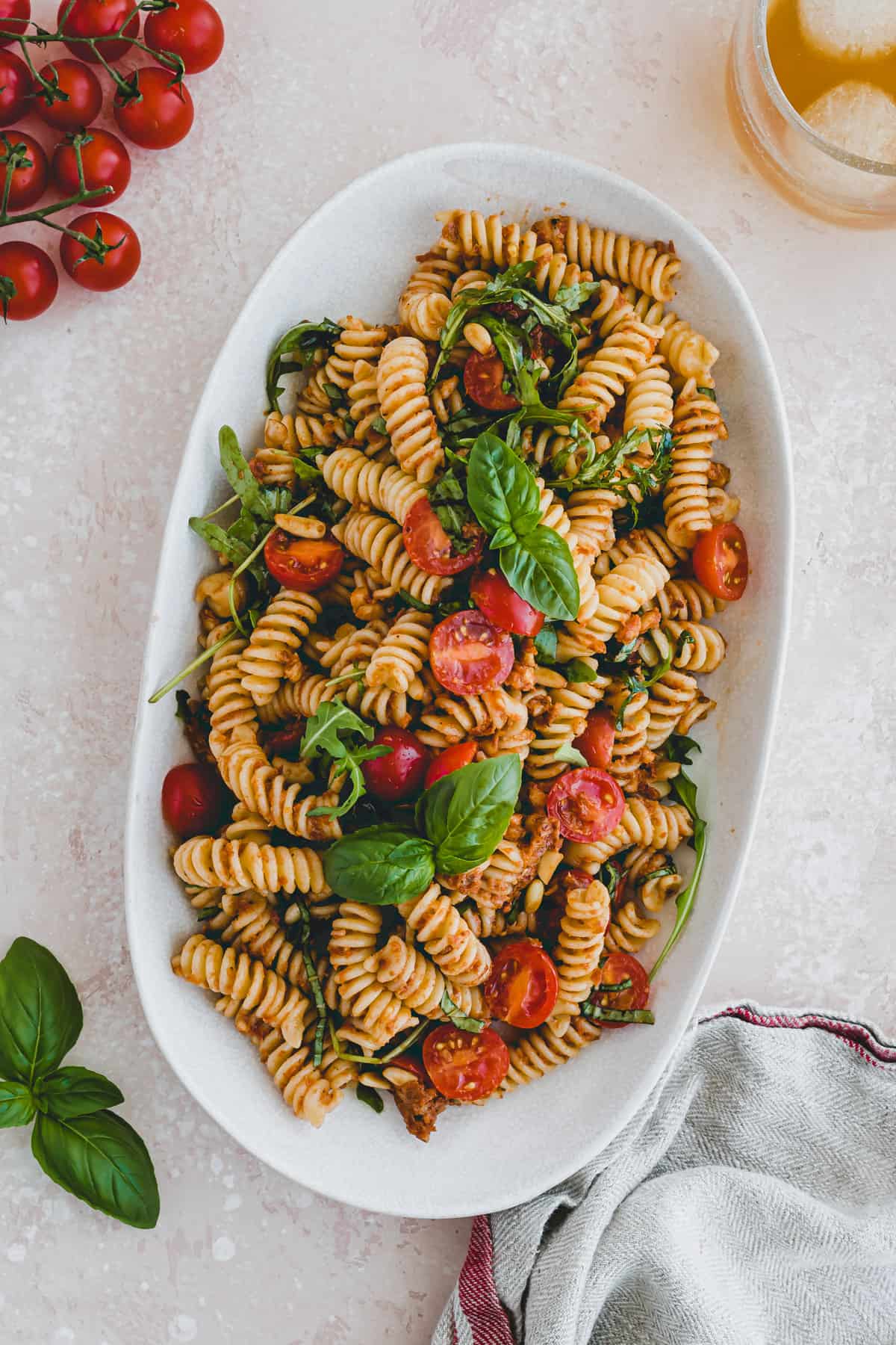 vegan pasta salad with pesto rosso, arugula, and tomatoes on a serving platter