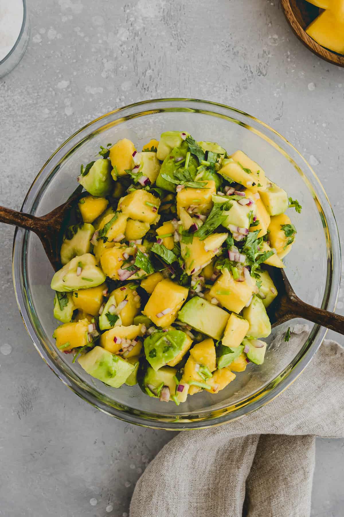 Top view of a glass bowl filled with avocado mango salad with wooden spoons in it for serving. 