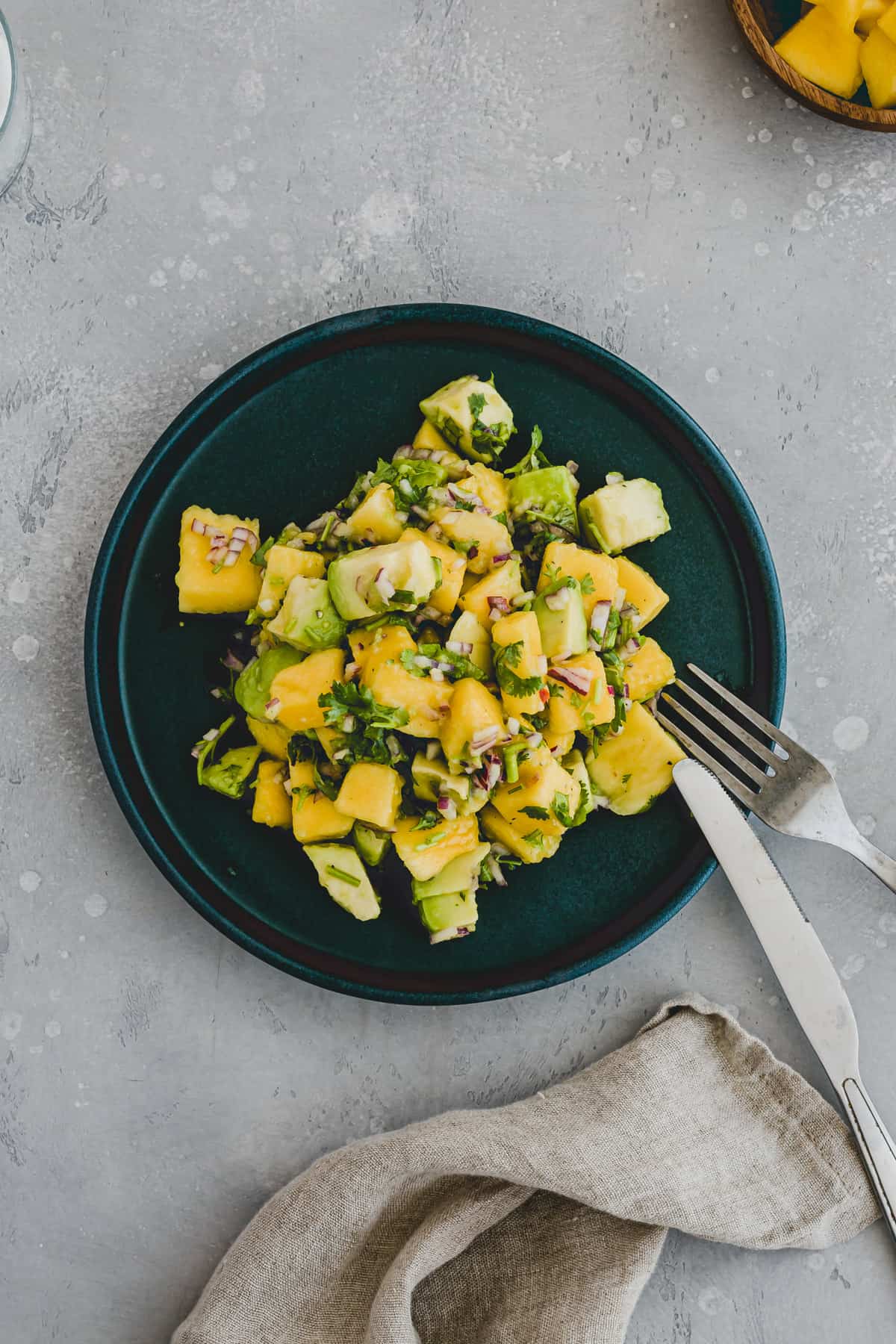 Top view of a teal plate with mango avocado salad on it with a knife and fork on the edge of the plate. 