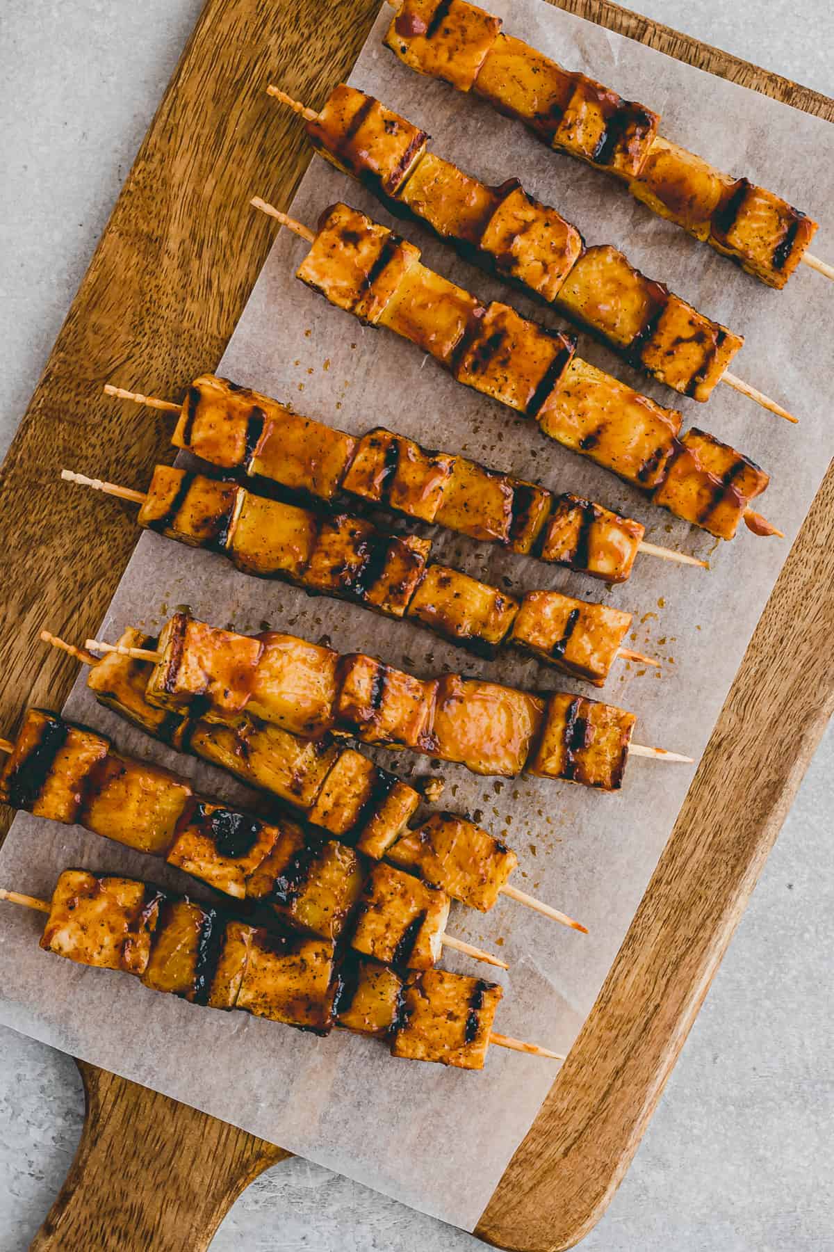 Top view of grilled BBQ tofu skewers on a wooden chopping board.