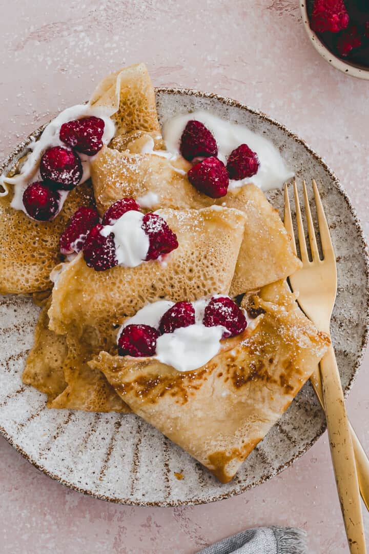 french crepes served on a plate with fresh raspberries
