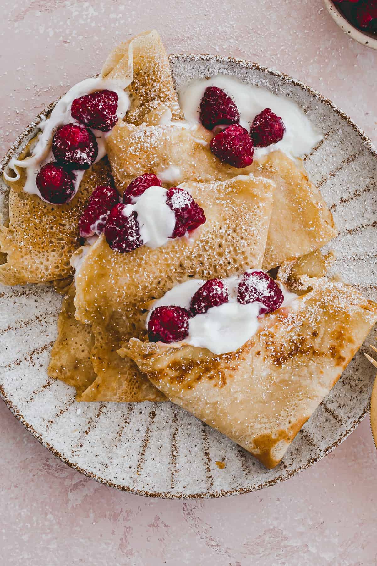 french crepes served with powdered sugar and raspberries