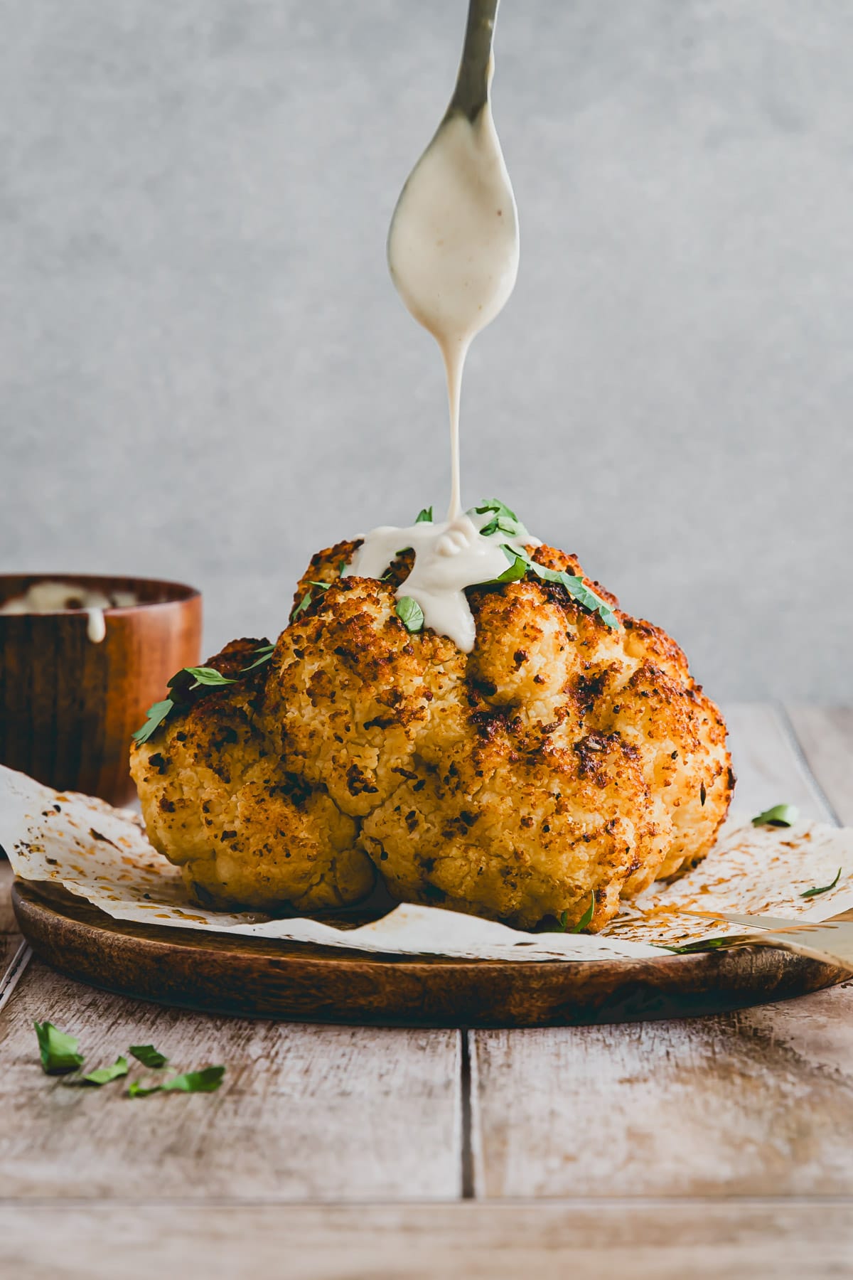 a spoon drizzling tahini sauce over a whole head of roasted cauliflower