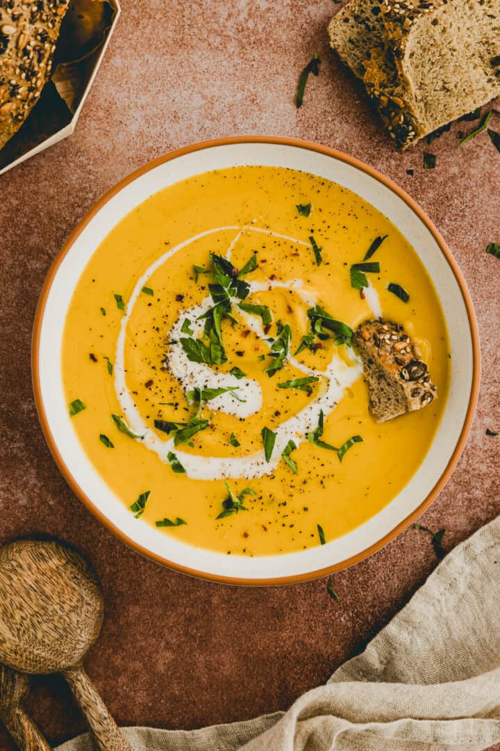 rote linsensuppe in einem teller mit petersilie dekoriert, brot liegt nebenan