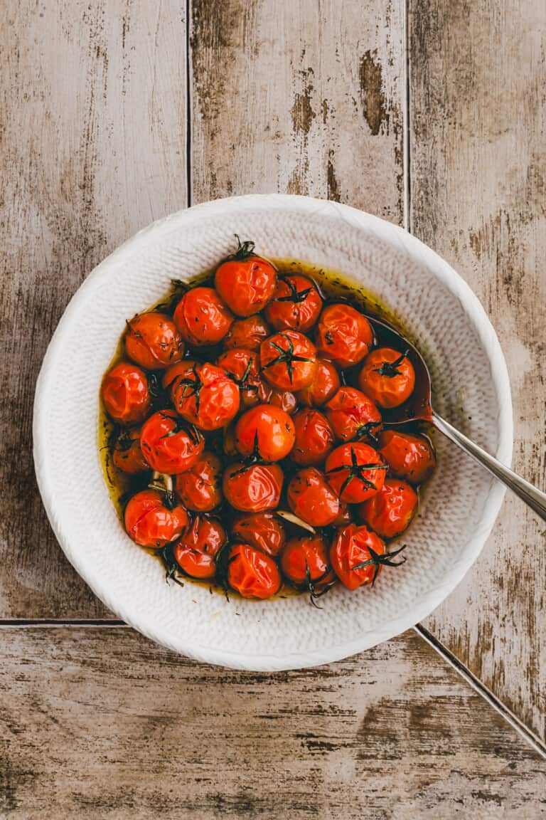 roasted cherry tomatoes in a white bowl with a spoon