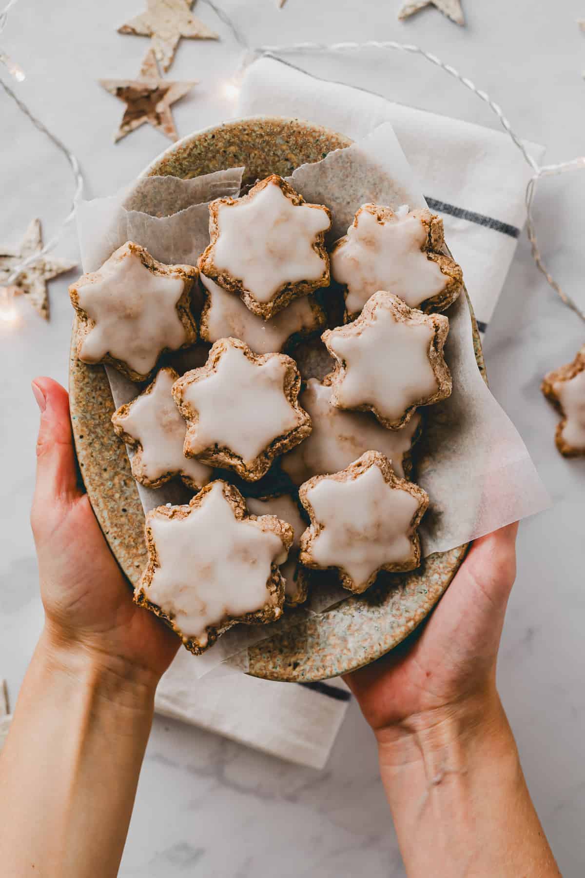 two hands holding a plate filled with german cinnamon star cookies