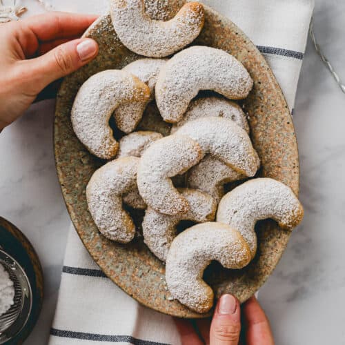 two hand holding a plate with Vegan Almond Crescent Cookies