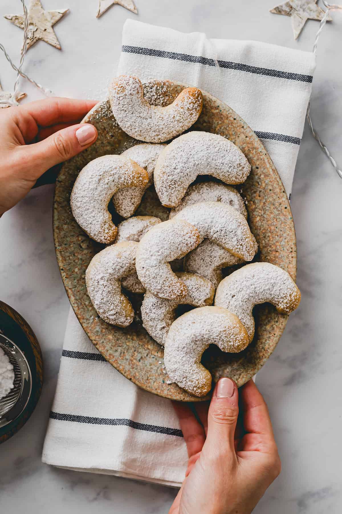 two hand holding a plate with Vegan Almond Crescent Cookies