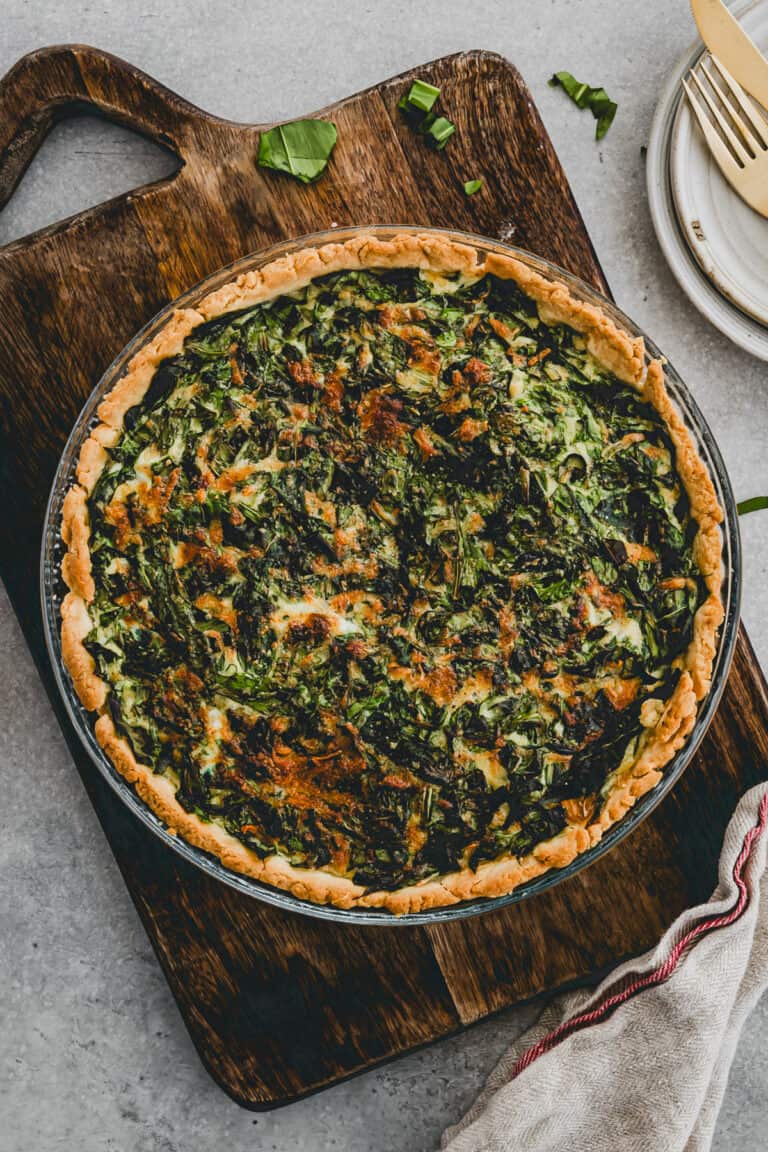 bärlauch quiche in einer tarteform auf einem holzbrett