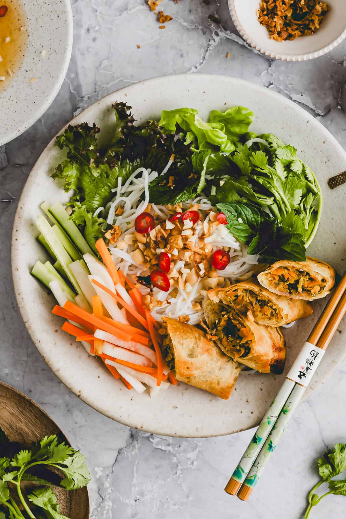 vietnamesischer reisnudelsalat mit frühlingsrollen in einem teller mit stäbchen