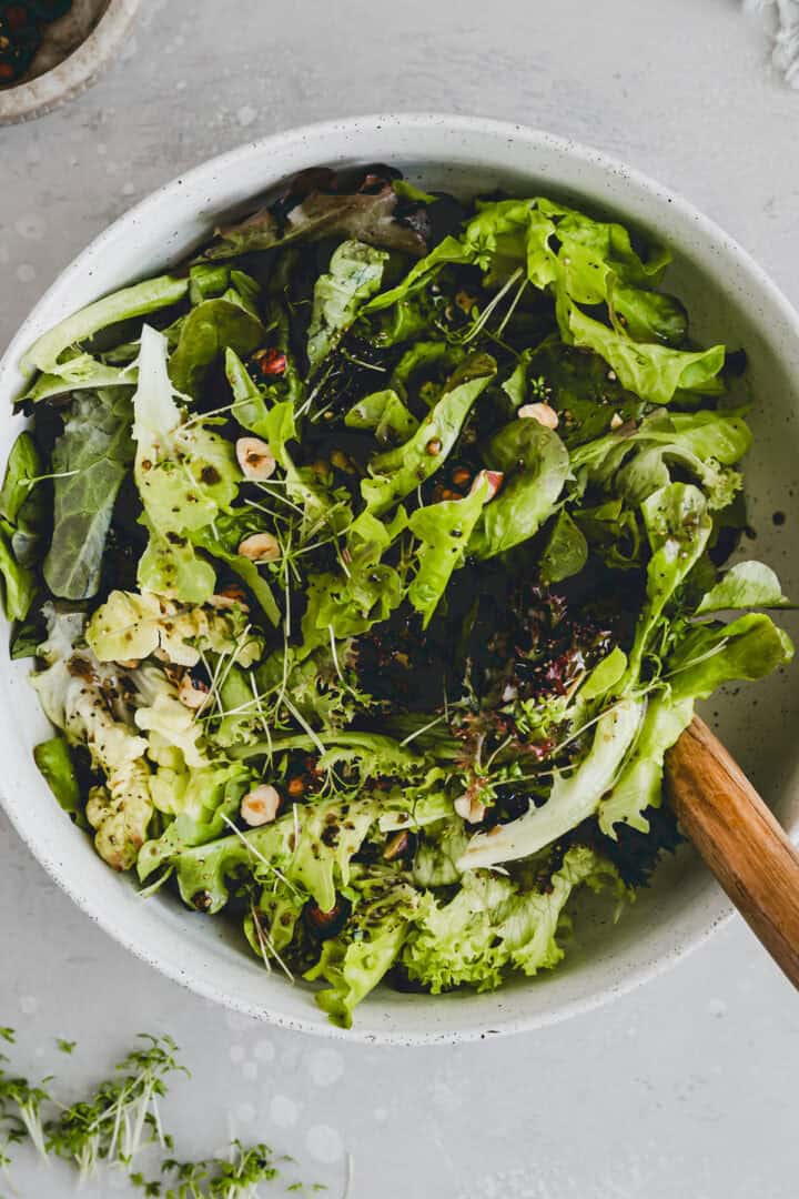 eine schüssel gefüllt mit grünem salat, haselnüssen, und einem balsamico vinaigrette