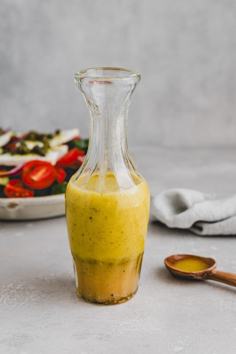 greek salad dressing in a glass bottle next to a greek salad