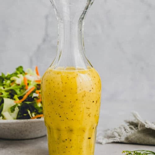 white balsamic vinegar in a glass bottle next to a mixed green salad