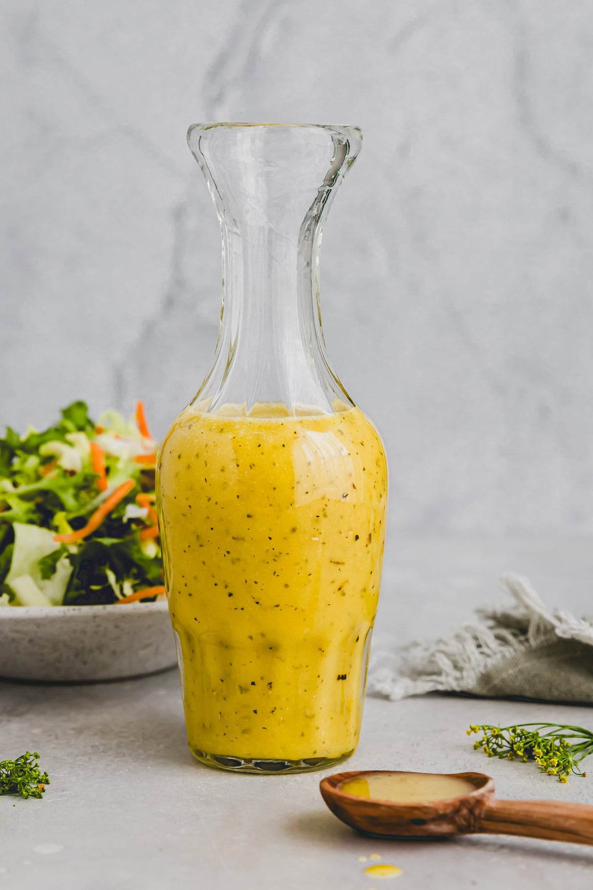 white balsamic vinegar in a glass bottle next to a mixed green salad
