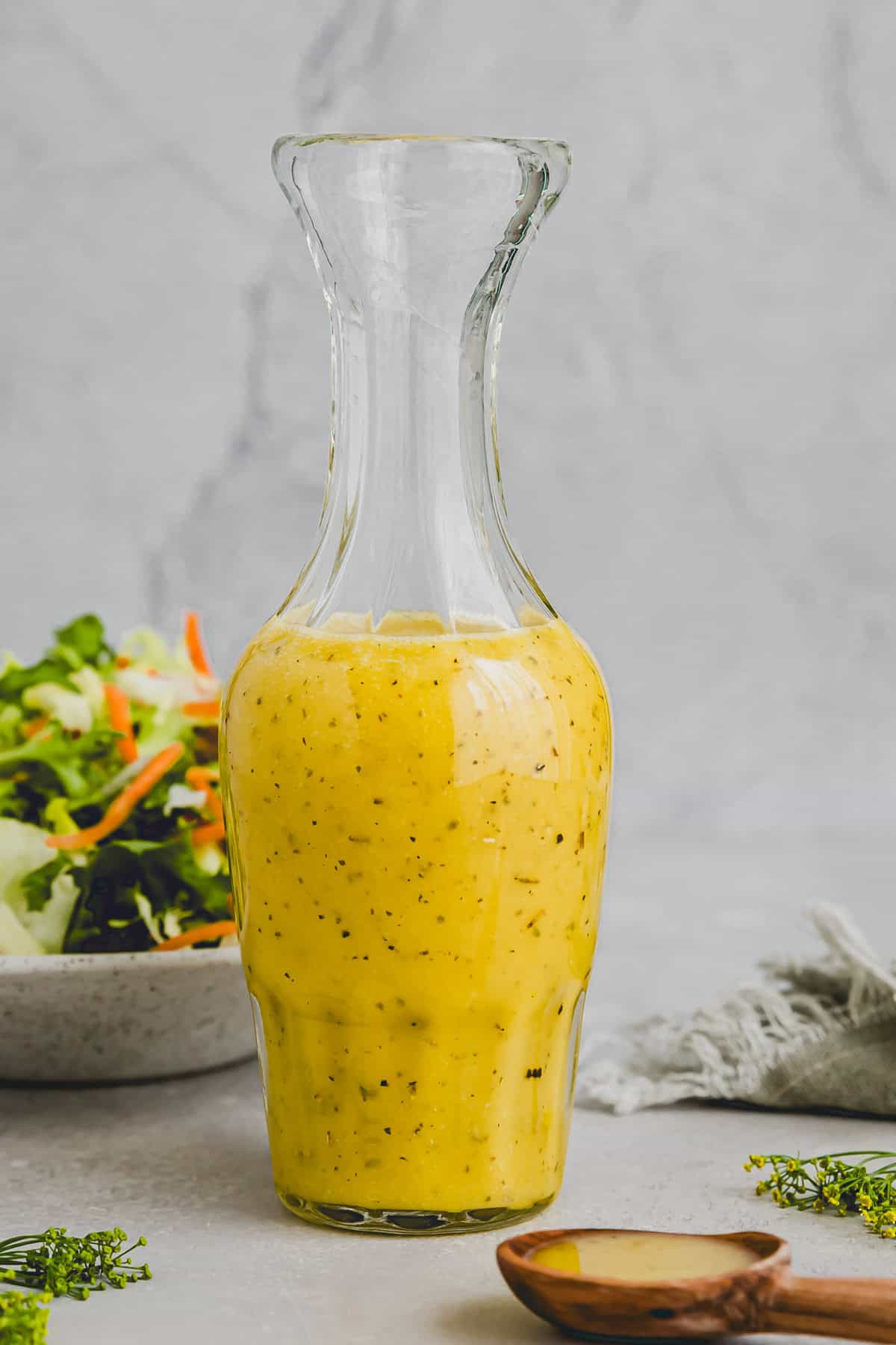 white balsamic vinegar in a glass bottle next to a mixed green salad