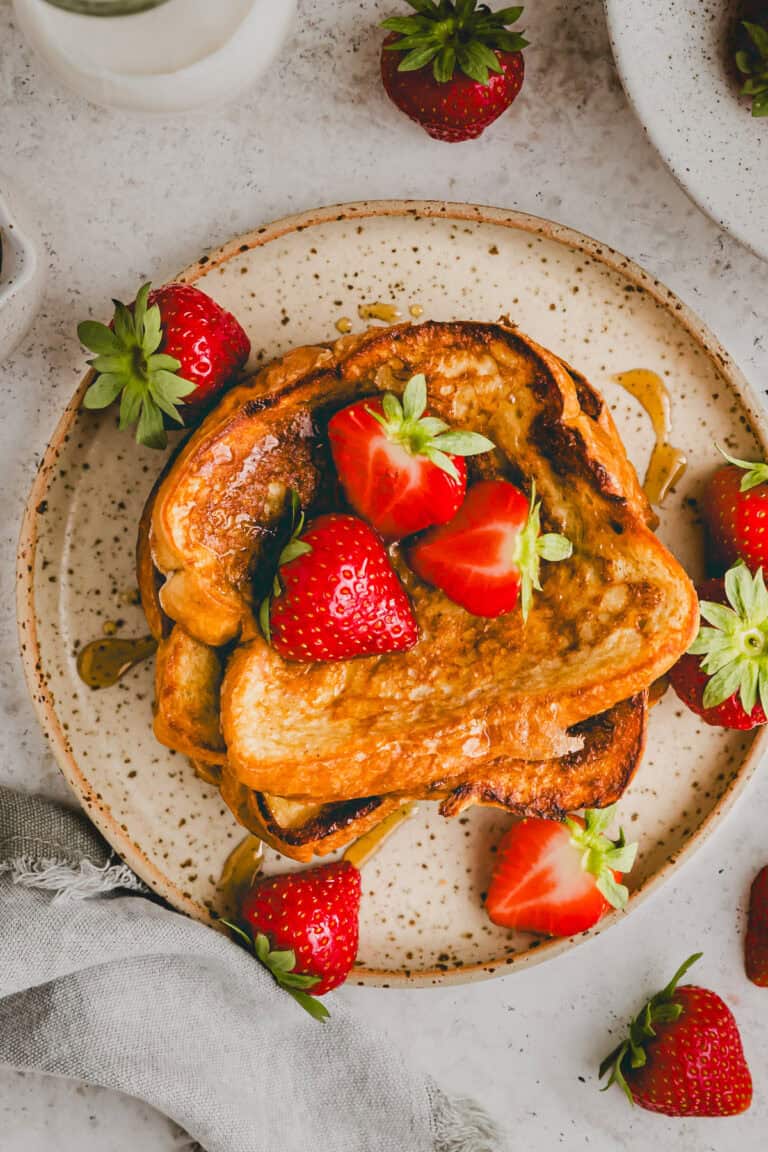 brioche french toast topped with fresh strawberries and maple syrup