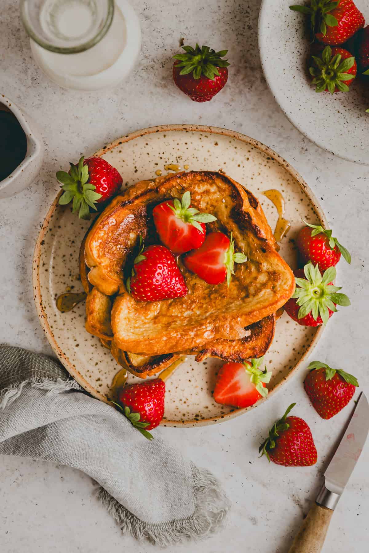 brioche french toast on a plate topped with strawberries and maple syrup