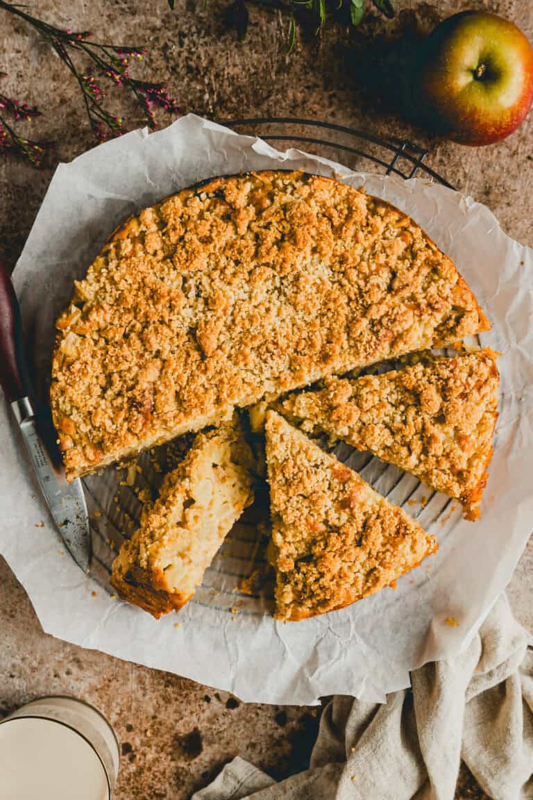 angeschnittener apfelkuchen mit streusel auf einem backpapier