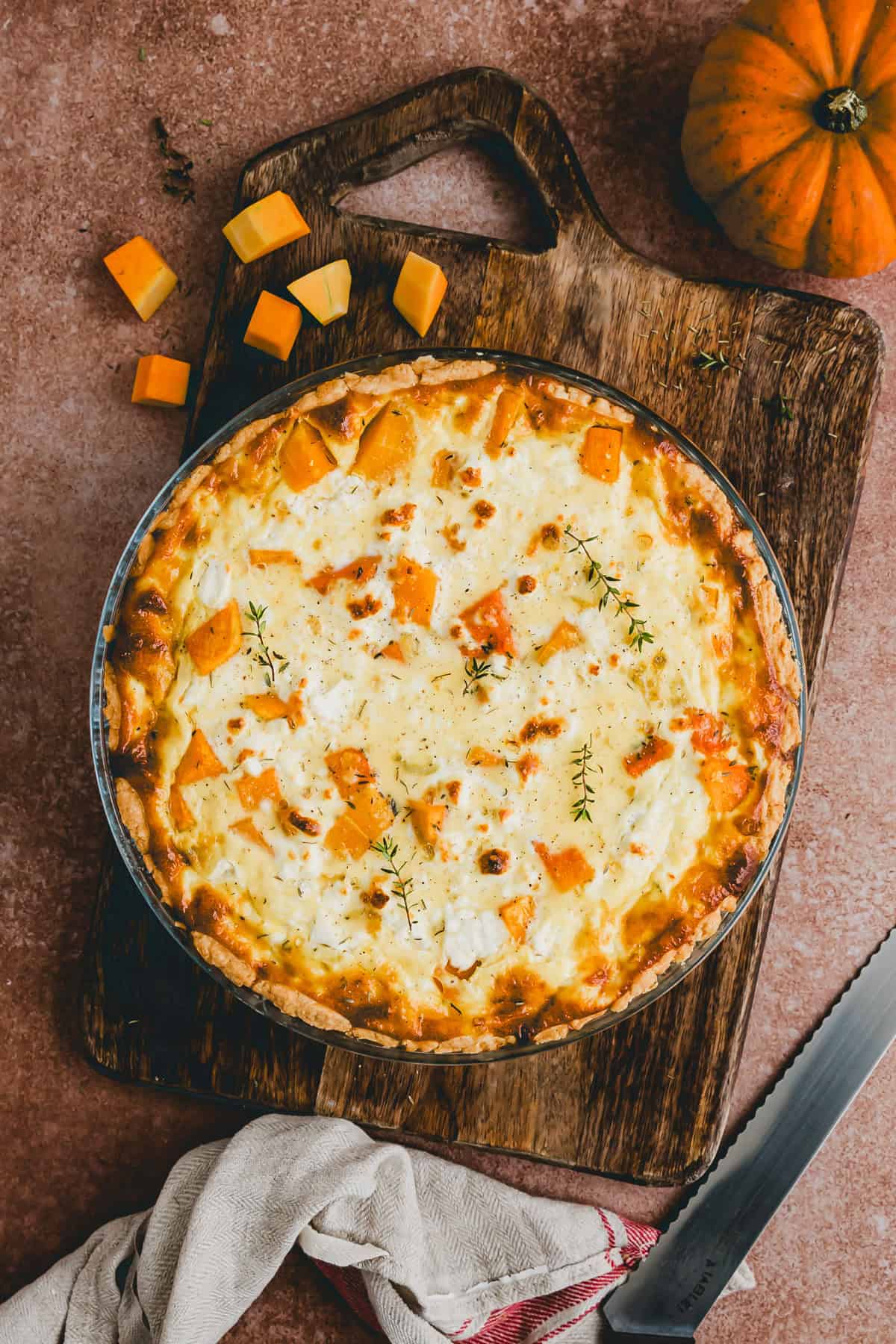 kürbis quiche mit feta in einer quiche form neben einem kürbis