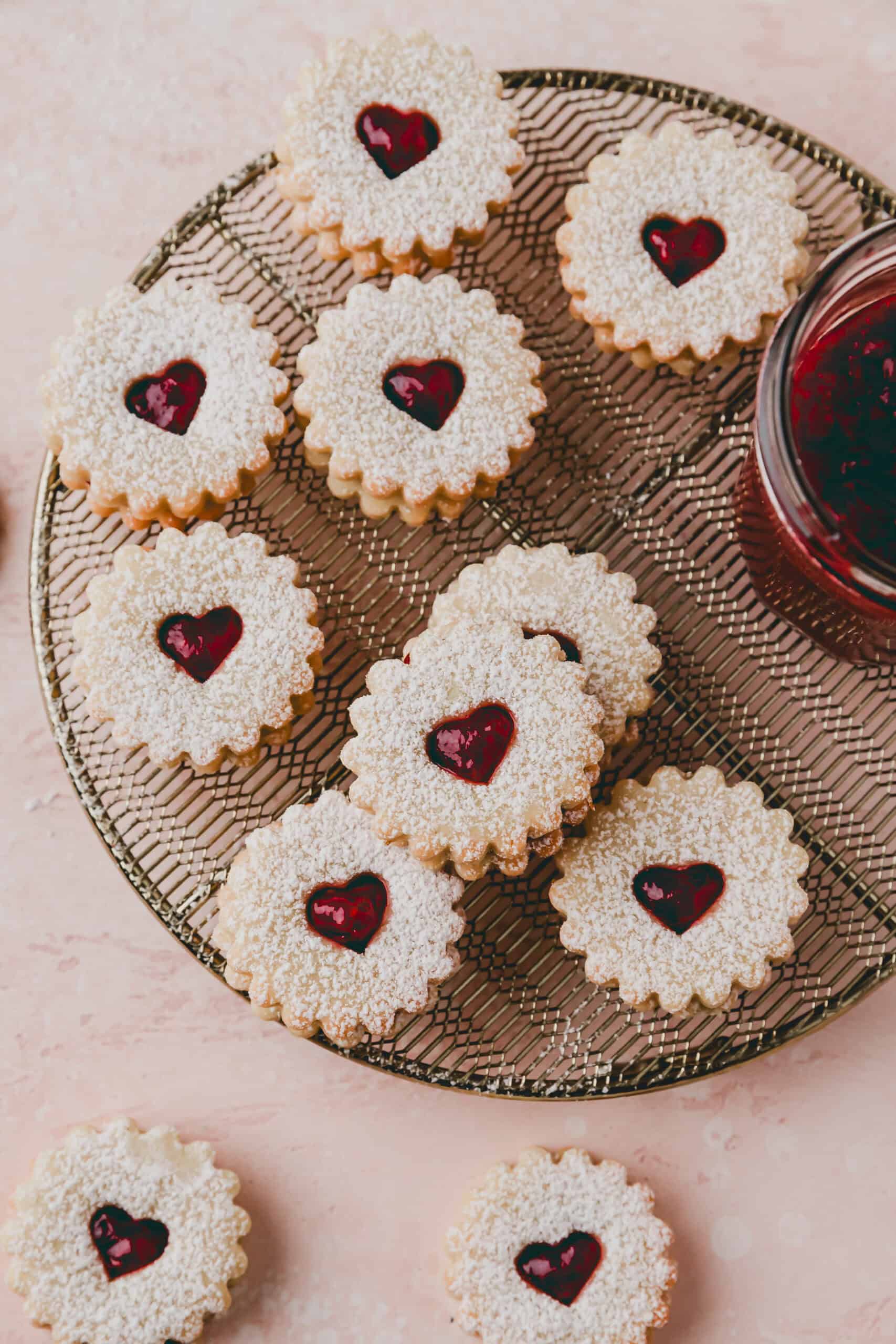linzer cookies on a golden wire rack covered wtih powdered sugar