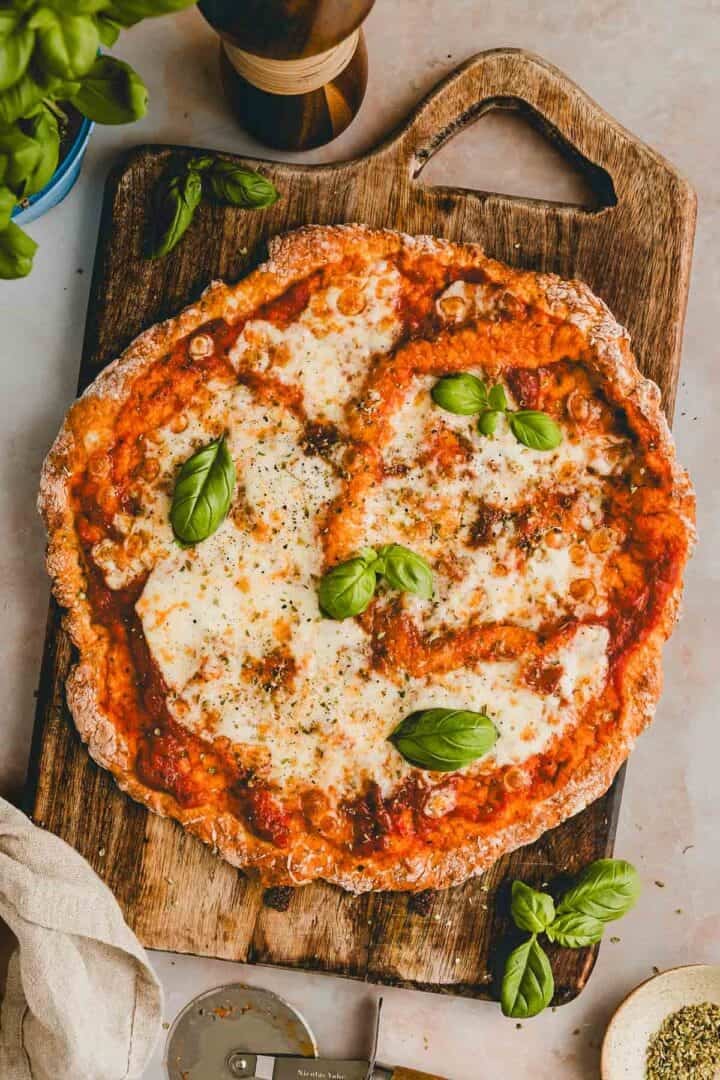 proteinpizza auf einem holzbrett mit frischem basilikum garniert