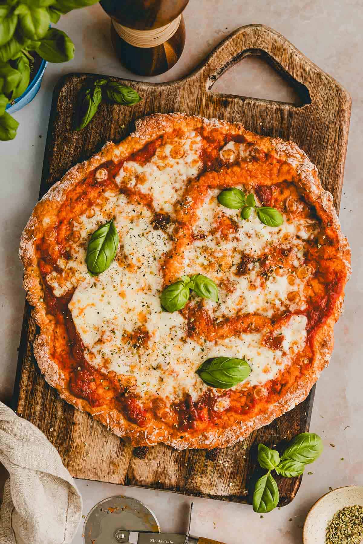 proteinpizza auf einem holzbrett mit frischem basilikum garniert