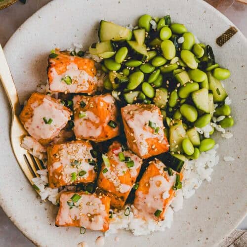 bang bang salmon bowl with cucumber edamame salad in a bowl with a golden fork