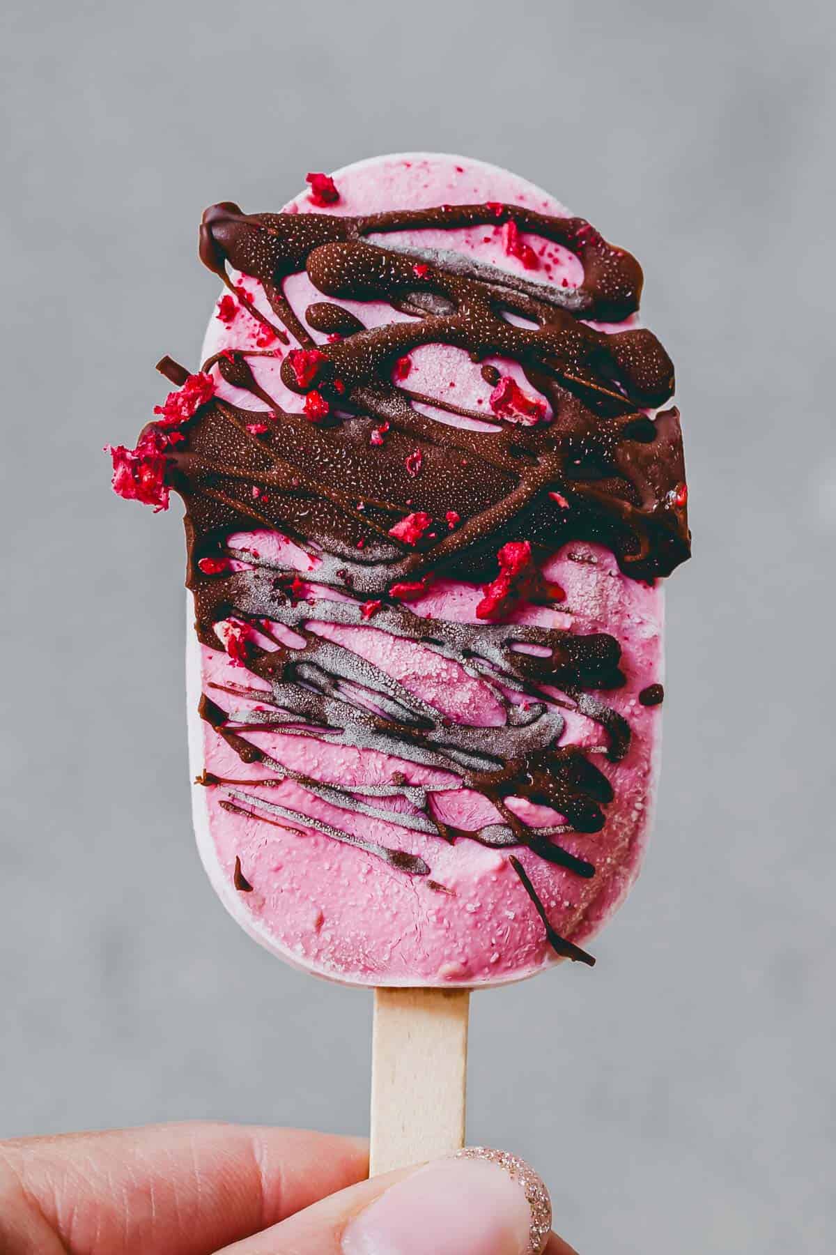 eine hand hält ein high protein eis am stiel mit schokolade überzogen