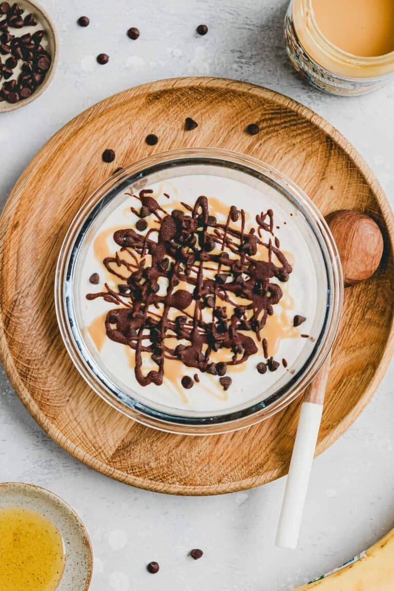 Banana Cottage Cheese Ice Cream in a glass container topped with melted chocolate, chocolate chips, and peanut butter