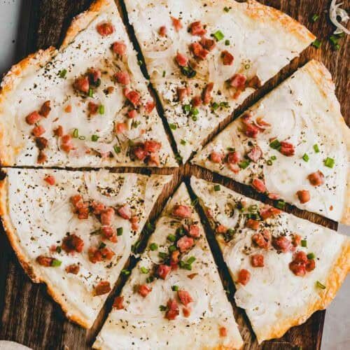 protein flammkuchen mit speck und zwiebeln belegt auf einem holzbrett