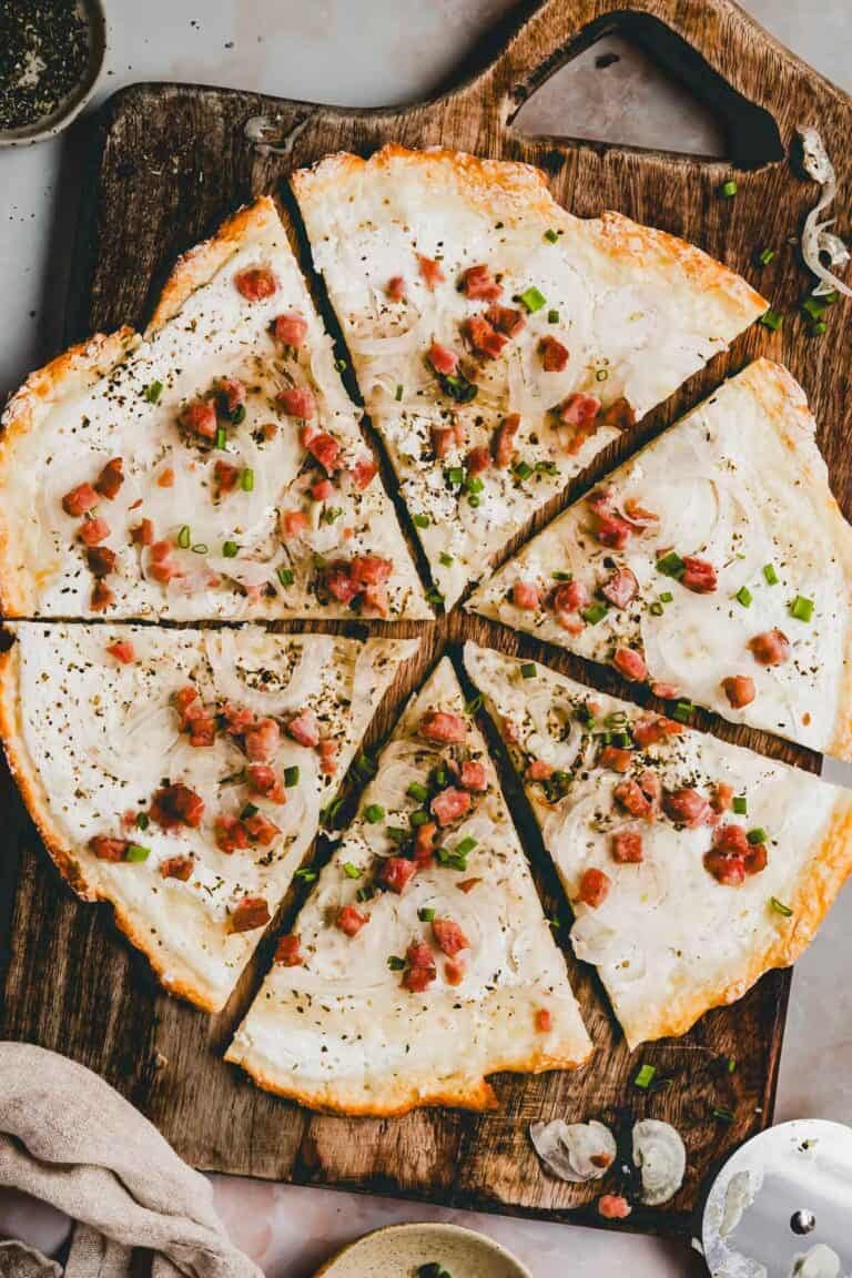 protein flammkuchen mit speck und zwiebeln belegt auf einem holzbrett