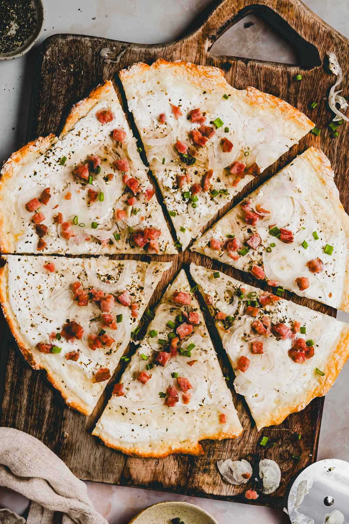 protein flammkuchen mit speck und zwiebeln belegt auf einem holzbrett