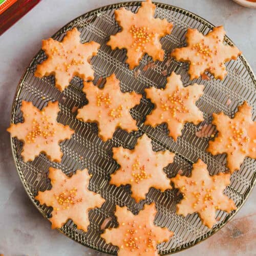 Aperol Plätzchen mit streudekor auf einem goldenen auskühlgitter neben einer flasche aperol